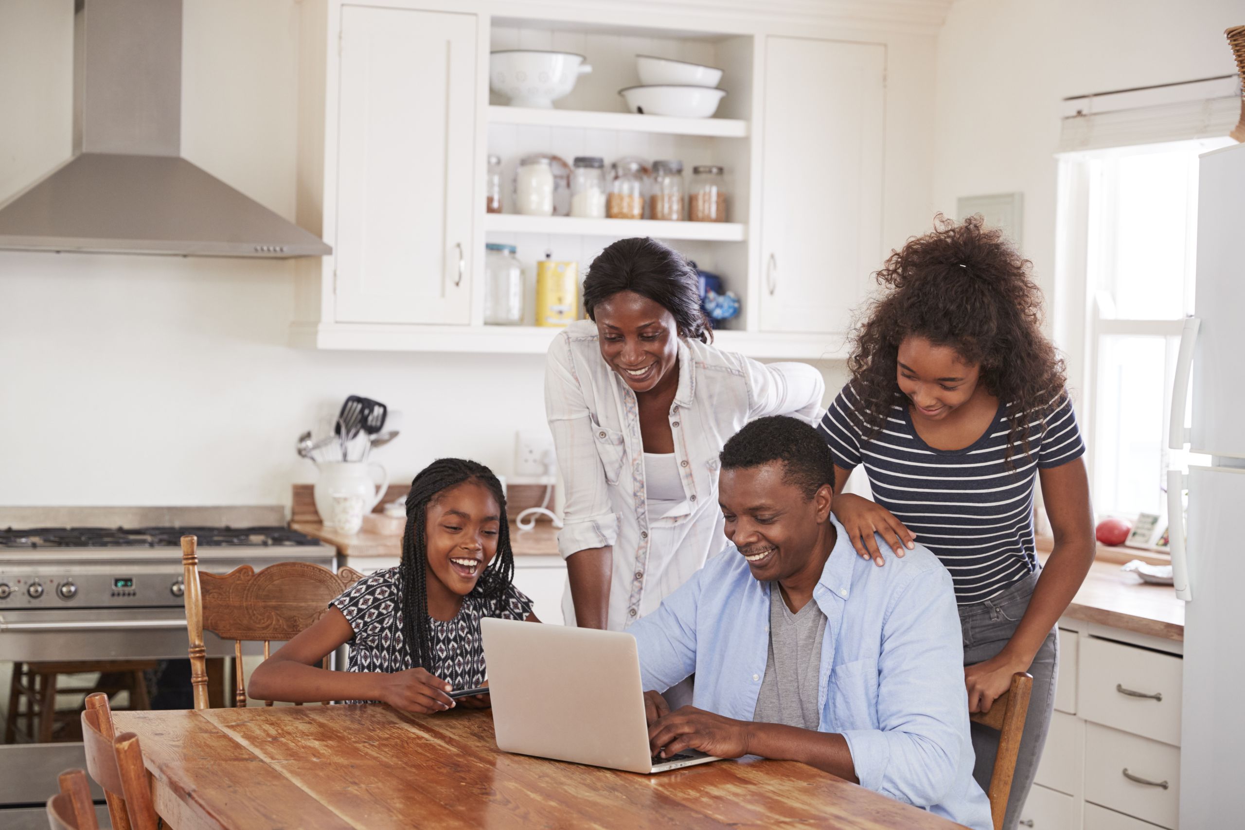 Family Around Kitchen Table On Laptop Together